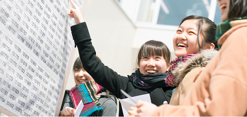 合格発表のボードの前で女の子が喜んでいる画像